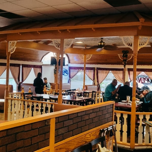 Restaurant interior with patrons dining in booths and at tables within a decorative wooden gazebo structure.