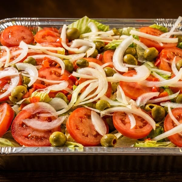 Fresh salad with lettuce, sliced tomatoes, onions, and green olives in a foil container.
