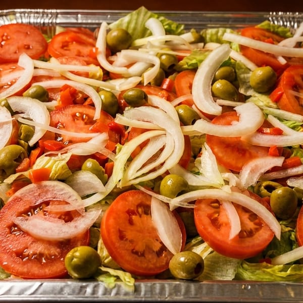 Fresh salad with sliced tomatoes, onions, green olives, and lettuce in a foil tray.