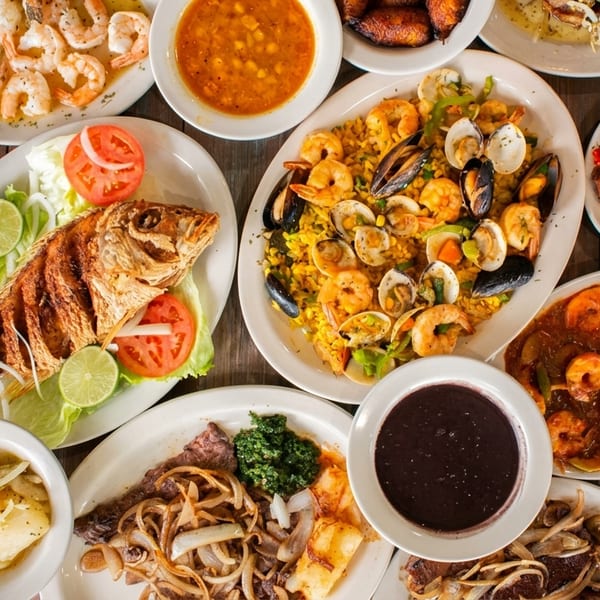 A vibrant spread of Cuban dishes, including whole fried fish, seafood paella, and various meat and shrimp plates.