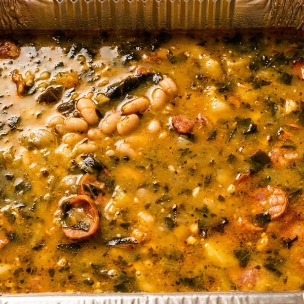 Hearty caldo verde soup with kale, white beans, and sausage in a foil takeout container.